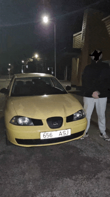 a man stands in front of a yellow car with the license plate 656 asj