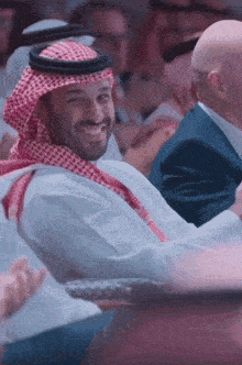 a man in a keffiyeh smiles while sitting in a crowd of people