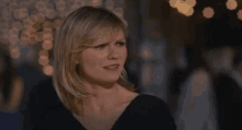 a woman in a black dress is standing in front of a crowd of people and making a funny face .