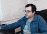 a man wearing glasses and a blue jacket is sitting in front of a computer .