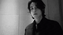 a black and white photo of a man in a suit standing in front of a wall .