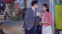 a man in a suit and tie is standing next to a woman in a pink sweater .