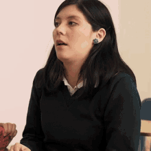 a woman wearing a black sweater and blue earrings looks to the side