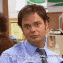 a man in a blue shirt and tie is sitting in an office and making a funny face .