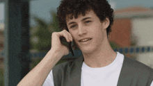a young man with curly hair is talking on a cellphone