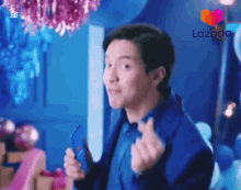 a man in a blue jacket is holding a cell phone and making a heart sign