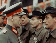 a group of men in military uniforms are standing in a line and one of them is wearing a red hat