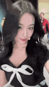 a woman with long black hair is wearing a black dress with a white bow