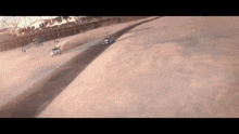 two cars are driving down a sandy road