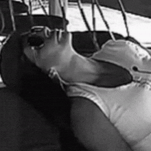 a black and white photo of a woman in a bathing suit laying on a boat .