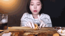 a woman wearing white gloves is eating chicken on a wooden cutting board .