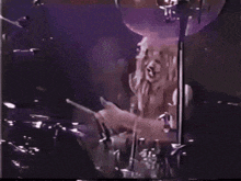 a person playing drums in a dark room with a purple background