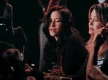 two women are sitting in a dark room with drinks in their hands