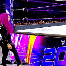 a woman with purple hair is walking out of a wrestling ring with the number 20 in the background .