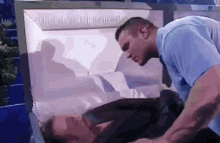 a man in a blue shirt is standing next to a coffin with a man in it .