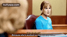 a woman in a blue sweater is sitting at a table in a courtroom talking to a man .