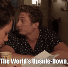 a man sits at a table reading a piece of paper with the words the world 's upside down below him