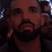 a man with a beard is sitting in a dark room looking up at something .