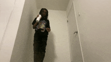 a person standing in a hallway holding a white cup and a black shirt with a cartoon on it