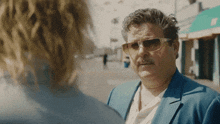 a man in a blue suit and sunglasses talks to a woman