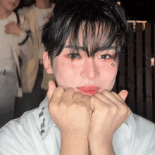 a young man with makeup on his face making a heart with his hands