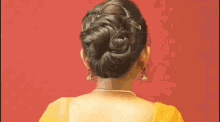 the back of a woman wearing a yellow blouse and a bun .