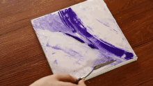 a person is using a spatula to spread purple paint on a white surface