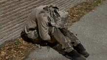 a person is kneeling down on the sidewalk with a hood on their head .