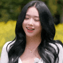 a woman with long black hair wearing a white shirt and a gold necklace smiles with her eyes closed