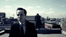 a man in a suit and tie is standing on a rooftop looking down at something