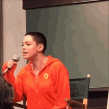 a woman with a shaved head is holding a microphone and talking into it .