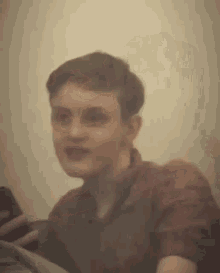 a young man in a red shirt is sitting on a couch talking to someone .