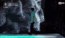 a man in a blue shirt is walking on a stage in front of a screen that says mnet