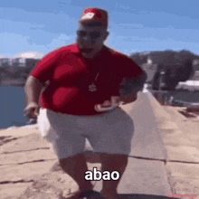 a man in a red shirt and white shorts is standing on a beach with the word abao written on the ground