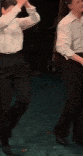 two men in white shirts and black pants are dancing together on a stage .