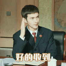 a man in a suit and tie is sitting at a desk with chinese writing on the top