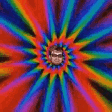a man wearing sunglasses and a rainbow sticker on his forehead is smiling .