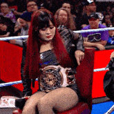 a woman with red hair is sitting in a chair in a wrestling ring with a belt around her waist