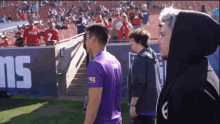 a man in a purple shirt is standing in front of a wall that says ns