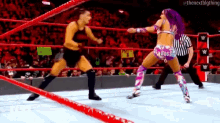 two women are wrestling in a wrestling ring while a referee watches .