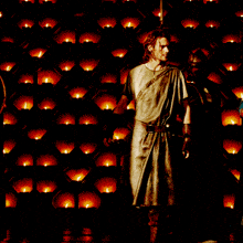 a man in a toga stands in front of a wall of lit candles