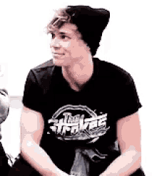 a young man wearing a black t-shirt and a black beanie is sitting on a bench .