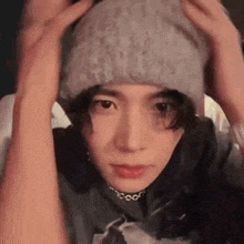 a young man wearing a beanie and a choker is holding his head .