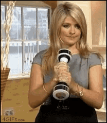 a woman is holding a dumbbell in her hands and smiling .