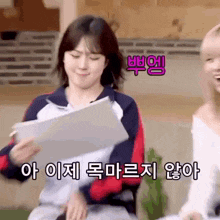 a woman is holding a piece of paper in her hand while another woman looks on .