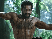 a shirtless man in a forest with the letters kvvcsr on the bottom right