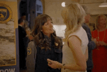 two women are standing next to each other at a party and talking .