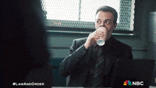 a man in a suit and tie drinking a cup of coffee from a paper cup