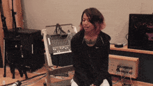 a woman in a black nike jacket sits in front of a mixer in a recording studio