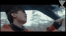 a man in an orange jacket is driving a car with the word uni3 on the bottom right